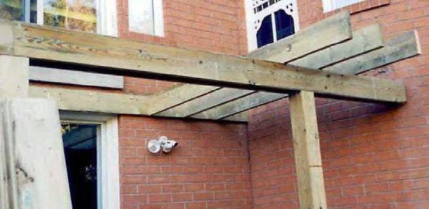 Framing for a second story deck with posts, beams, and some deck joists installed.